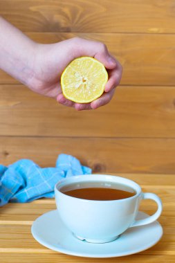 Beyaz arka planda çay, fincan ve çay tabağı, beyaz ahşap bir masada çay ve limonlu bir fincan. Erkek eli bir limon ve bir fincan çay tutuyor..