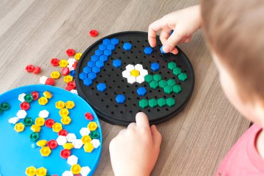 Beyaz tişörtlü küçük sarışın kız evde ya da anaokulunda plastik renkli mozaikle oynuyor. Erken eğitim kavramı