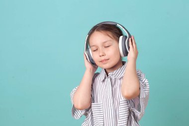 Bir kız mavi arka planda kulaklıkla müzik dinliyor. Sevimli bebek gözlerini kapayarak mutlu dans müziğinden hoşlanıyor.
