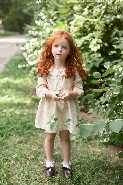 Uma menina de 4 anos de idade com cabelos longos encaracolados está brincando ao ar livre em um parque da cidade. Uma criança bonita olha para a câmera com um olhar sério. — Fotografia de Stock