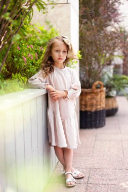 Retro elbisesi ve kafasında büyük bir fiyonk olan sevimli küçük bir kız güneşli bir yaz gününde şehirde dolaşıyor. Mutlu çocuklar sokakta gülümsüyor..