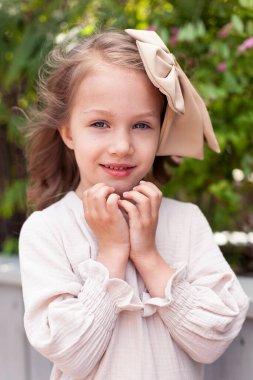 Retro elbisesi ve kafasında büyük bir fiyonk olan sevimli küçük bir kız güneşli bir yaz gününde şehirde dolaşıyor. Mutlu çocuklar sokakta gülümsüyor..