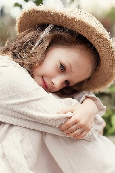 Engraçado bonito menina de 5-6 anos de idade, em um vestido bege e um chapéu de palha, posando em um parque contra o fundo da natureza. Felicidade. A estação de verão. — Fotografia de Stock