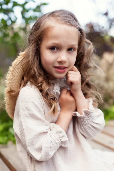 Chica linda divertida de 5-6 años, en un vestido beige y un sombrero de paja, posando en un parque sobre el fondo de la naturaleza. Felicidad. La temporada de verano. — Foto de Stock