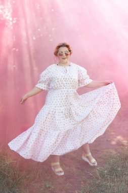 Genç ve mutlu bir kadın bir yaz günü çıplak ayakla elinde ayakkabılarla bir tarlada yürüyor. Model artı beden. seçici odak.