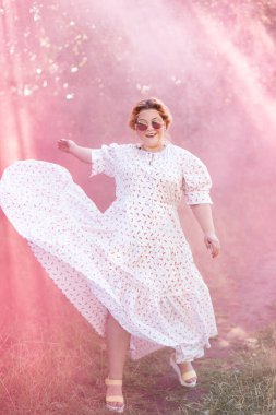 Zarif beyaz elbiseler giyen genç ve güzel bir kadın. Ormanda bir gülümsemeyle dikiliyor.