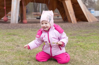 Pembe ceketli küçük engelli bir kız ve bahar günü yeşil çimlerde sürünen bir şapka. Seçici odaklı bir resim.