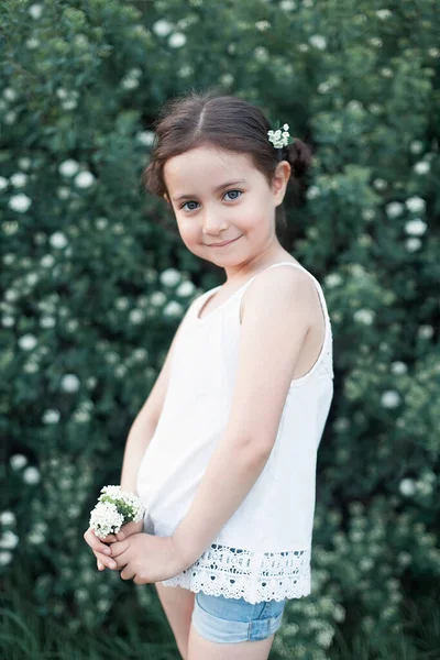 Маленькая девочка держит в руках букет белых цветов и улыбается в камеру. Искренний момент полного счастья. Гармония в природе — стоковое фото