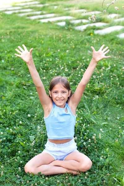 Uma menina sorridente na grama verde no parque da cidade em um dia de verão. passeios ao ar livre. — Fotografia de Stock