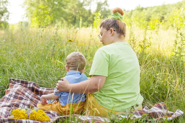 Portrait d'un charmant petit garçon handicapé couché dans les bras de sa mère aimante sur l'herbe verte du parc. invalidité. Les mères aiment. Soutien familial. — Photo