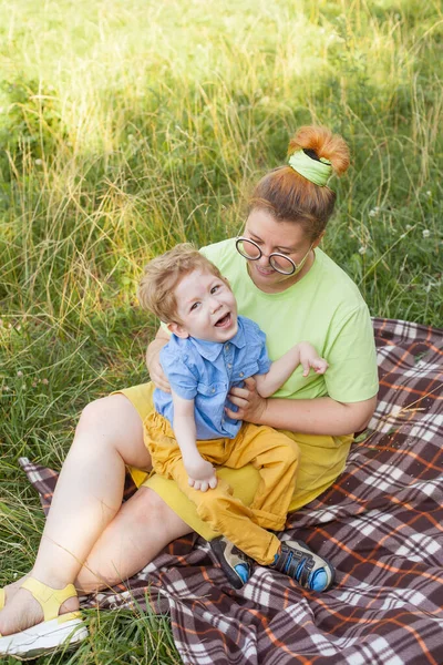 A mother with a young disabled son is resting in a city park on a sunny day. Infantile cerebral palsy. Disability. Rehabilitation of a disabled child. Socialization of a disabled person. — Stock Photo, Image