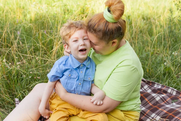 Porträt einer Mutter, die ihren kleinen Sohn mit besonderen Bedürfnissen in einem Sommerpark umarmt. Behinderungen. Kindheitslähmung. Sommerspaziergänge an der frischen Luft. — Stockfoto