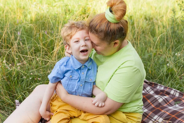 Retrato de una madre abrazando a su hijo pequeño con necesidades especiales en un parque de verano. Incapacidad. Parálisis infantil. Paseos de verano al aire libre. Fotos de stock