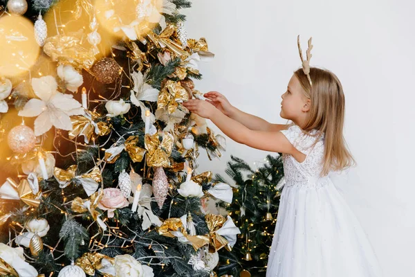 A five-year-old girl is decorating a Christmas tree. Children, family and holiday concept. Christmas tree at home. Have a good mood on New Years Eve. Concept preparation to New Year holidays