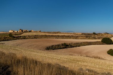 Yakın zamanda ekilen tarlaların arka planında yarı tahrip edilmiş koyun bağları ve Moncayo zirvesi var.