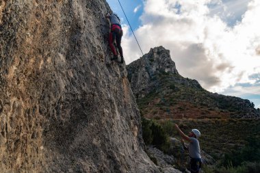 Tırmanış ekipmanlarıyla dağcı kız neredeyse tırmanma rotasının sonuna ulaşırken partneri onu aşağıdan bağlıyordu.