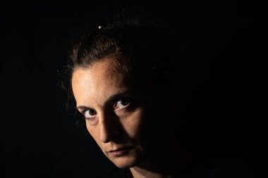 Çok loş bir kadının karanlık profil portresi. Kadın ileriye bakıyor, güvensizlik ya da üzüntü hissi veriyor.