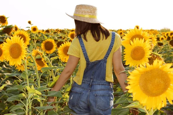 Girl in denim overalls and yellow t-shirt on a background of sunflowers
