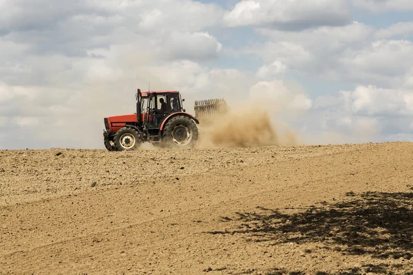 Tractor arando un campo con un rastro de polvo detrás de él Fotos De Stock Sin Royalties Gratis