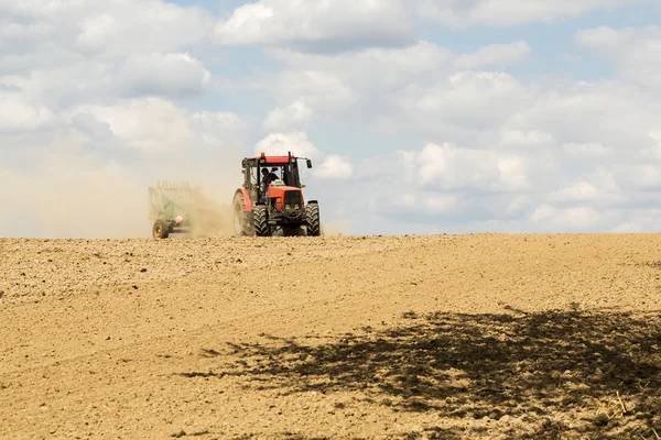 Tractor arando un campo con un rastro de polvo detrás de él Imagen De Stock
