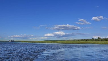 Huzurlu yaz manzarası. Mavi nehir yeşil bankalar arasında akar. Gökte bulutlar var. Gemi uzaklıktan görülebilir. Botswana 'da. Chobe..