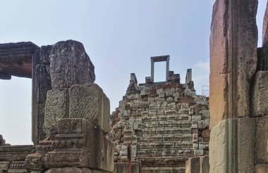Angkor tapınağının kalıntıları. Ön planda harap olmuş süs duvarları var. Kalenin tepesine çıkan merdivenler ve gökyüzüne açılan açık kapı daha da görünür. Kamboçya.
