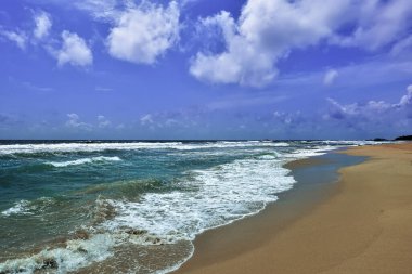 Hint Okyanusunda Sörf. Narin köpüklü turkuaz dalgalar kumsalda yuvarlanıyor. Gök kubbede resim gibi bulutlar var. Yaz günü. Sri Lanka.