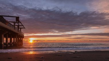 İyi akşamlar. Güneş denizin üzerinde alçaktan parlıyor. Mavi bulutlar pembeyle vurgulanır. Suda güneşli bir yol var. Kumsalda köpüren dalgalar. Sol tarafta boş bir iskele var. Düş! Rusya