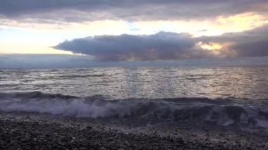 Yağmurdan önce gün batımı. Güneş, kara bulutların arasındaki boşluktan parlıyor. Dalgalar kumsaldaki çakıl taşlarında yuvarlanıyor. Su berrak, çelik bir gölgesi var. Karadeniz. Sonbahar.