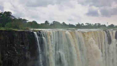 Zambezi Nehri platodan geçerek vadiye akar ve ünlü Victoria Şelalesi 'ni oluşturur. Güçlü su akıntıları sisle çevrilidir. Tropikal bitki örtüsü civarında. Gökyüzündeki bulutlar.