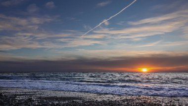 İyi akşamlar. Alacakaranlık. Mavi günbatımı gökyüzünde beyaz bulutlar, uçak pisti. Güneş batıyor. Kumsal çakıl taşlarında köpüren küçük deniz dalgaları. Karadeniz