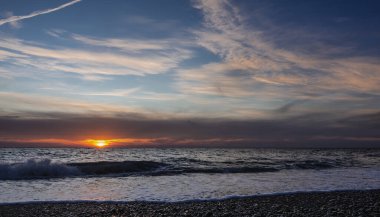 Akşam deniz manzarası. Gökyüzündeki sirk bulutları. Ufkun üzerinde batan güneşten gelen turuncu bir ışık var. Kumsalın çakıl taşları üzerine köpüklü bir dalga yayılır. Karadeniz.