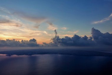 Boğazın üzerinde şafak söküyor. Mavi gökyüzünde, altın sirrus ve mor kümülüs bulutları. Pürüzsüz bir su yüzeyinde yansıma. Sahilde evlerdeki ışıklar görülebilir. İstanbul. Türkiye