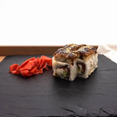 İçinde susam tohumları serpiştirilmiş bir ejderha sürüsü tepside servis tabağının üzerinde duruyor. Yakınlarda kırmızı turşulu zencefil ve peçete var. Beyaz arkaplan