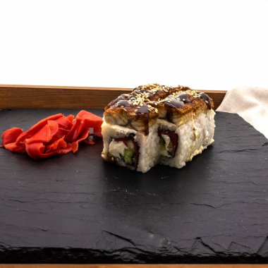 İçinde yılan balığı, peynir, salatalık ve susam tohumları olan bir ejderha sürüsü. Yakınlarda kırmızı turşulu zencefil ve peçete var. Beyaz arkaplan.