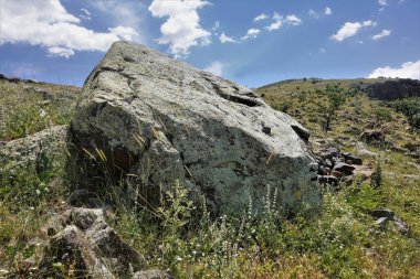 Tepelerin ve mavi gökyüzünün zeminine karşı kocaman manzaralı bir kaya yığını. Taş dokusu. Yeşil çimenler, her yer kır çiçekleri. Kapadokya manzarası. Türkiye