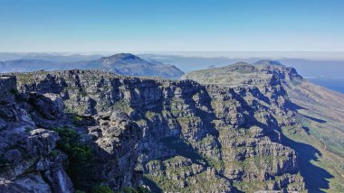 Cape Town 'daki Masa Dağı' nın zirvesinden bir dağ manzarası. Küçük yeşil bitki örtüsüyle kayalık yamaçlar ve zirveler. Tepelerin etrafındaki bulutlar. Güney Afrika