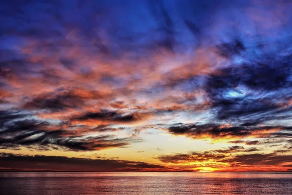 Fantastic, bright sunset over the sea. The clouds in the blue sky are highlighted in pink, scarlet, gold. Reflection on the calm surface of the water. Black Sea