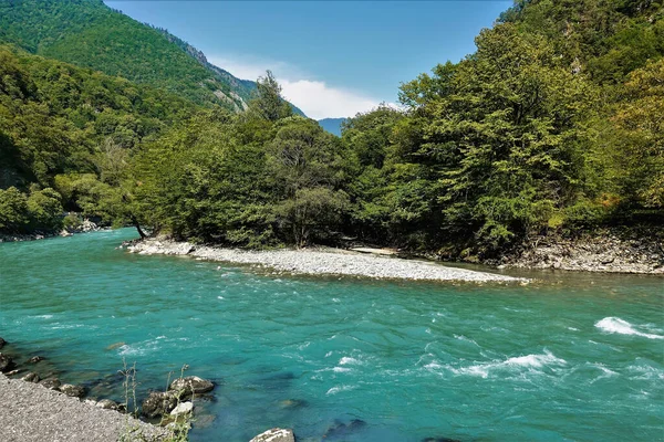 Yeşil dağ yamaçları arasında turkuaz bir nehir akıyor. Su köpürüyor. Ağaçlar kayalık adada yetişir. Yaz güneşli bir gün. Abhazya