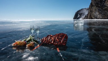 On the glistening smooth ice of the lake, there are two champagne glasses, red and yellow tulips and a decorative wicker heart. In the distance, a transparent ice splinter, picturesque rocks. Baikal clipart