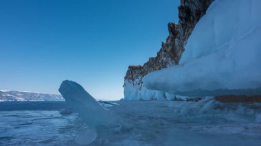 Buzla kaplı gölün yüzeyinde tuhaf hummozlar vardır. Kayanın tabanı donmuş. Uzakta, karla kaplı dağlar. Mavi gökyüzü. Kış güneşli bir gün. Baykal Gölü
