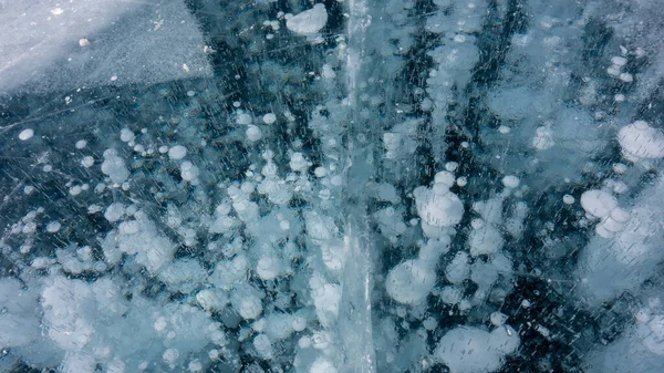 In the thickness of the transparent turquoise ice, white gas bubbles frozen in the form of columns are visible. Cracks on the surface. Full screen. Close-up. Lake Baikal