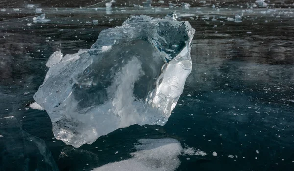 Shiny transparent shard of ice close-up. Sharp edges, bizarre shape. Reflection on the smooth frozen surface of the lake.