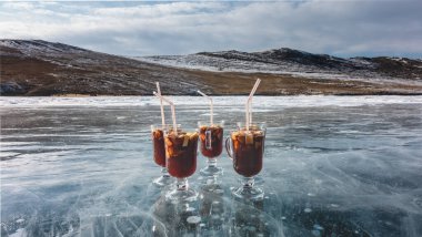 Glass mugs with mulled wine stand on a frozen lake. Red wine, sliced fruits, tubules. The ice is transparent, with cracks and gas bubbles in the depths. Background - snow-covered hills, sky. Baikal clipart