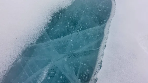 얼어붙은 호수의 표면은 눈으로 깨끗하고 청록색 얼음이 갈라지고 얼어붙은 수있다 — 스톡 사진