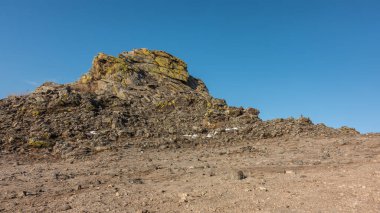 Açık mavi gökyüzünün arka planına karşı bir kaya. Taşlar arasında derin çatlaklar, sarı kertenkeleler görünür. Olkhon Adası