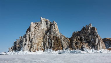 Donmuş bir gölün buzunun üzerinde, berrak mavi bir gökyüzünün zeminine karşı iki başlı, pitoresk bir kaya yükselir. Ayakta buz damlaları, buz saçakları. Baykal.