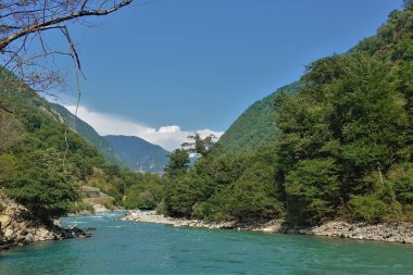 Turkuaz nehir yemyeşil bitki örtüsüyle dağ yamaçları arasında kıvrılarak akar. Suda su sıçraması var, köpük. Mavi gökyüzündeki bulutlar. Abhazya