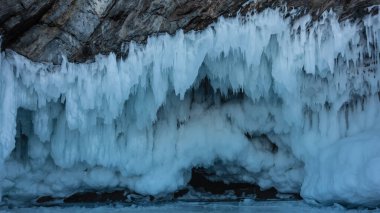 Buz saçakları birkaç sıra halinde kayanın tabanından sarkıyor, dantel fırçalar gibi. Yakın plan. Taş ve buz dokusu. Baykal Gölü, kış..