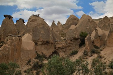 Mavi gökyüzüne karşı alışılmadık tuhaf kayalar. Üstleri mantar kapağı gibi. Vadide yeşil ağaçlar var. Resimli kümülüs bulutları. Kapadokya. Hindi. Yaz günü.